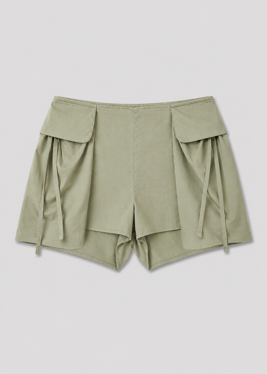 The Micro Pocket Short - Stone Green by Deiji Studios, with large front flap pockets and decorative side ties, is displayed laid flat on a white background.