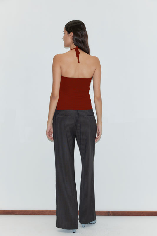 A woman stands facing away, wearing the Deiji Studios Half Top - Red and pinstriped black pants. She has long dark hair and is posed against a plain white background.