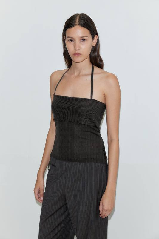 A woman with long brown hair stands against a plain white background with a neutral expression, wearing the Half Top - Black and pinstriped pants.