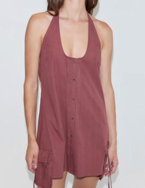 A woman wears the Pocket Halter Dress, a sleeveless, halter-neck, button-front mini in dusty rose with two side pockets and a loose, casual fit. Her head is partially out of frame.