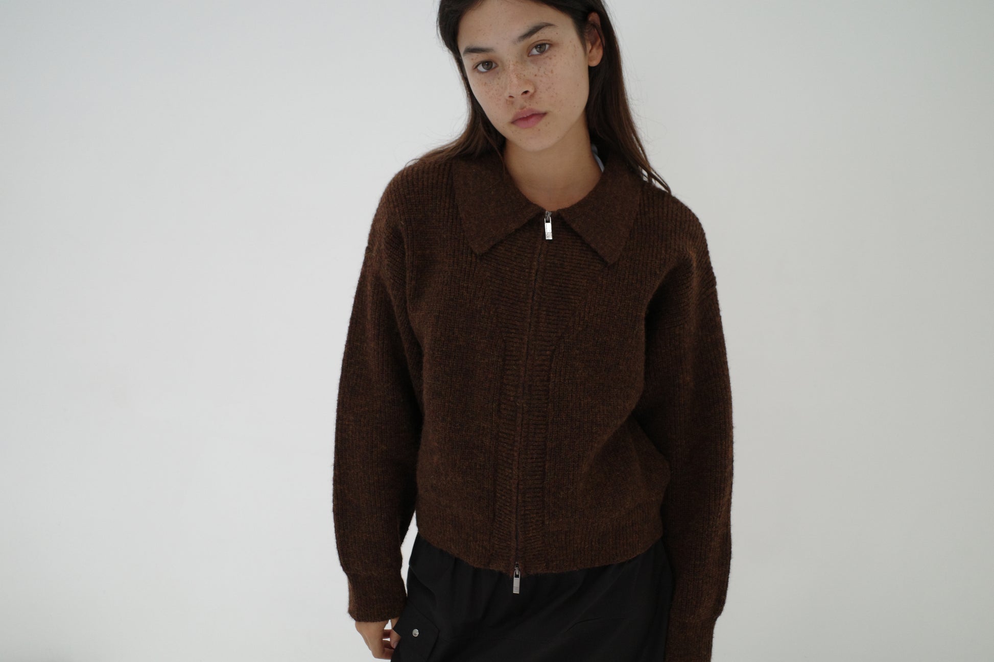 A young woman with long dark hair wears the Double Layer Cardigan - Brown from Deiji Studios and black pants, standing against a plain white background and looking directly at the camera with a neutral expression.