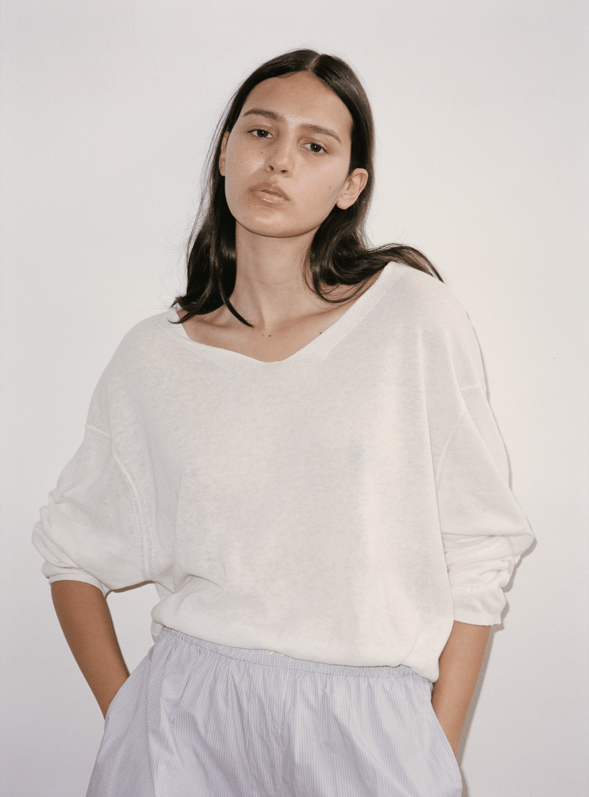 Close up shot of female model wearing Loose Knit Top in white by Deiji Studios. Top features woven neckline detail, dropped shoulder and seam detail. 