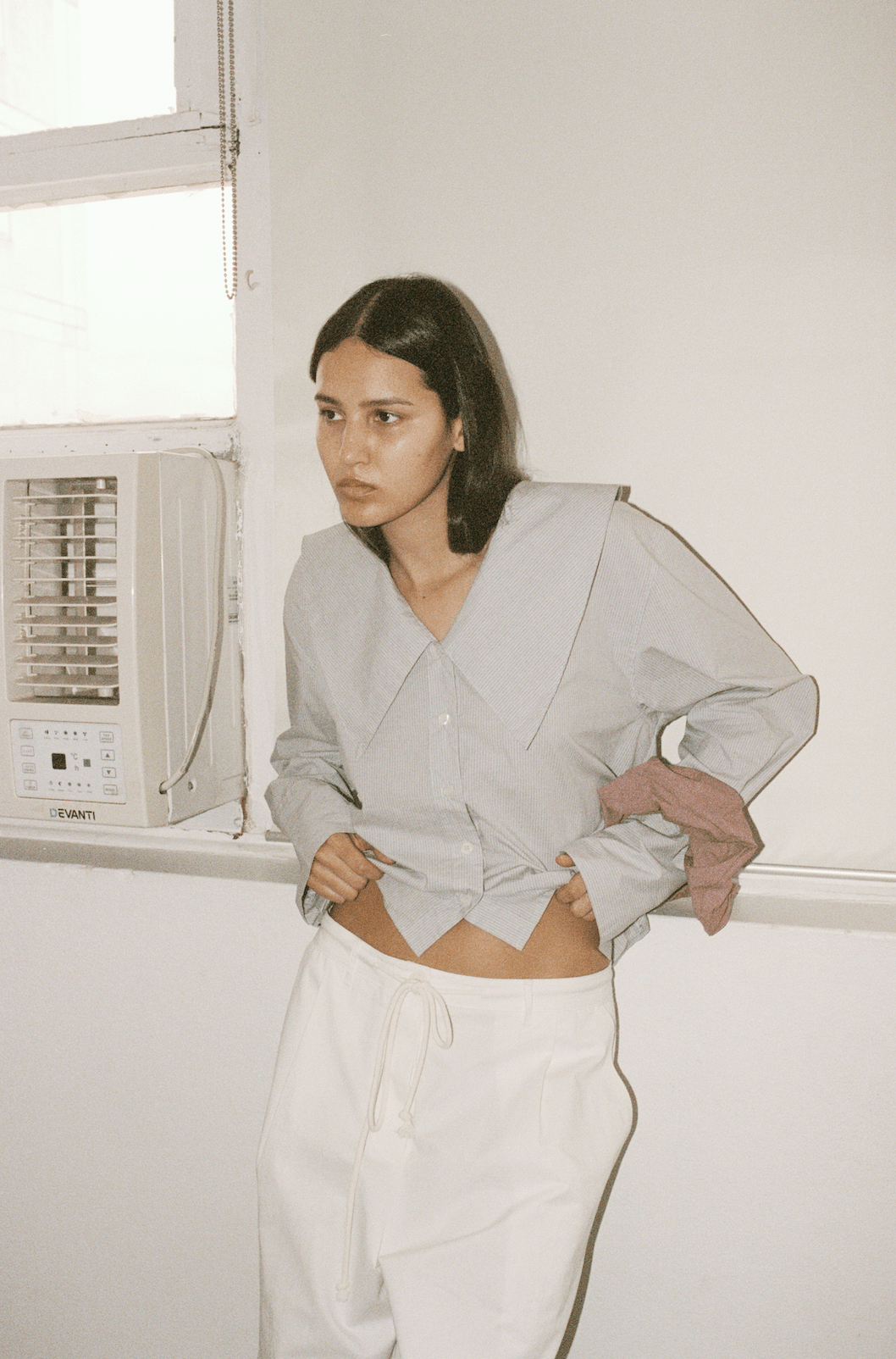 Film photo of model wearing the Oversized Collared Shirt in Dream Stripe, pulling shirt hem up to show drawcord waist detailing on Bartack Pants.