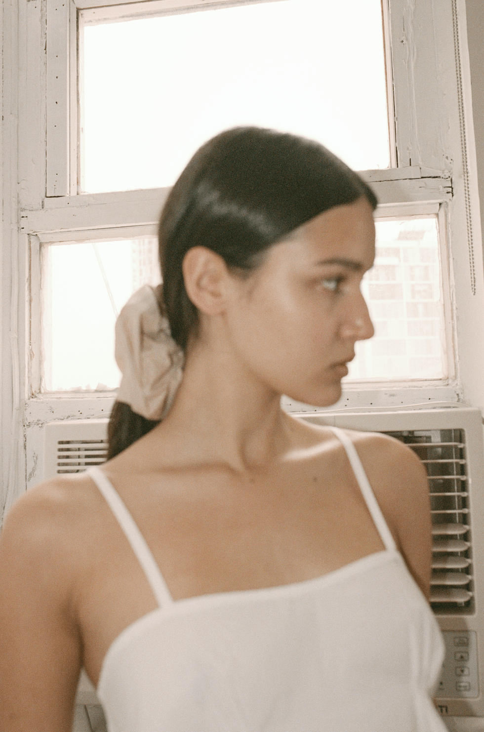 Close up film image of female model wearing Pleat Top in white and Scrunchie in sand stripe worn in hair.