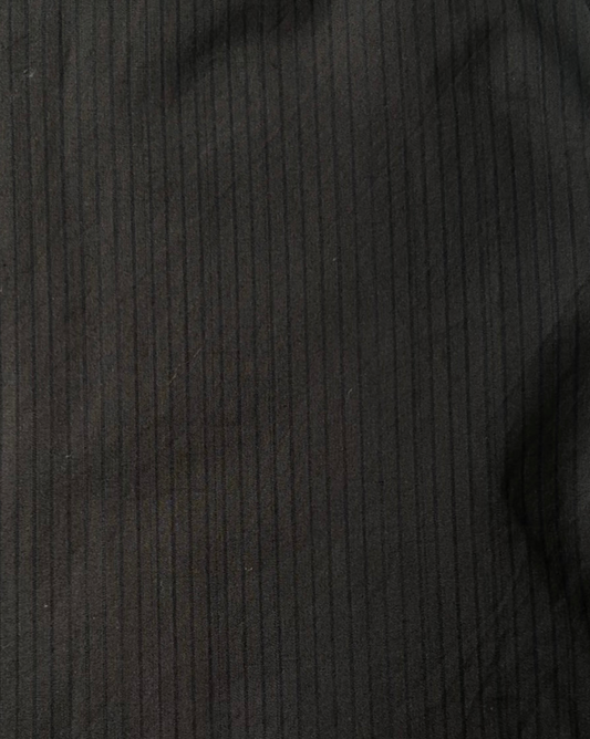 Close-up of the Layered Top - Black Stripe, made from dark organic cotton with subtle vertical pinstripes. The textured fabric features soft folds and shadows, highlighting its quality and style.