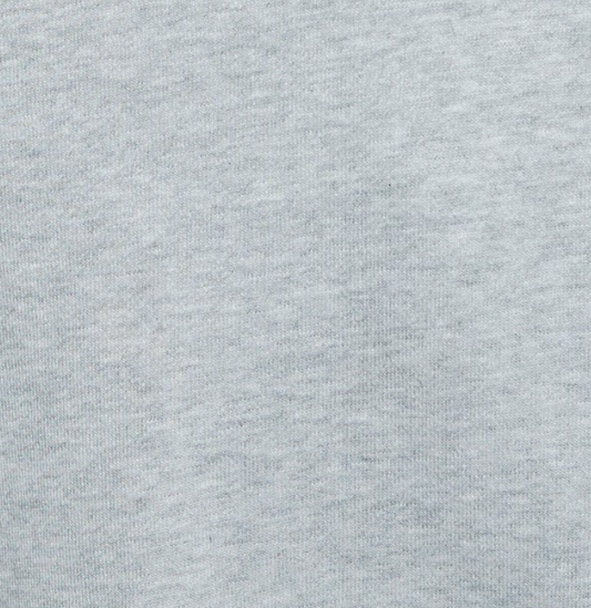 Close-up of light gray fabric with a soft, slightly mottled texture, reminiscent of the Jersey Jumper - Grey Marle. The surface displays subtle variations in shading that reveal the weave and fibers of the material. No distinct patterns or other objects are visible.