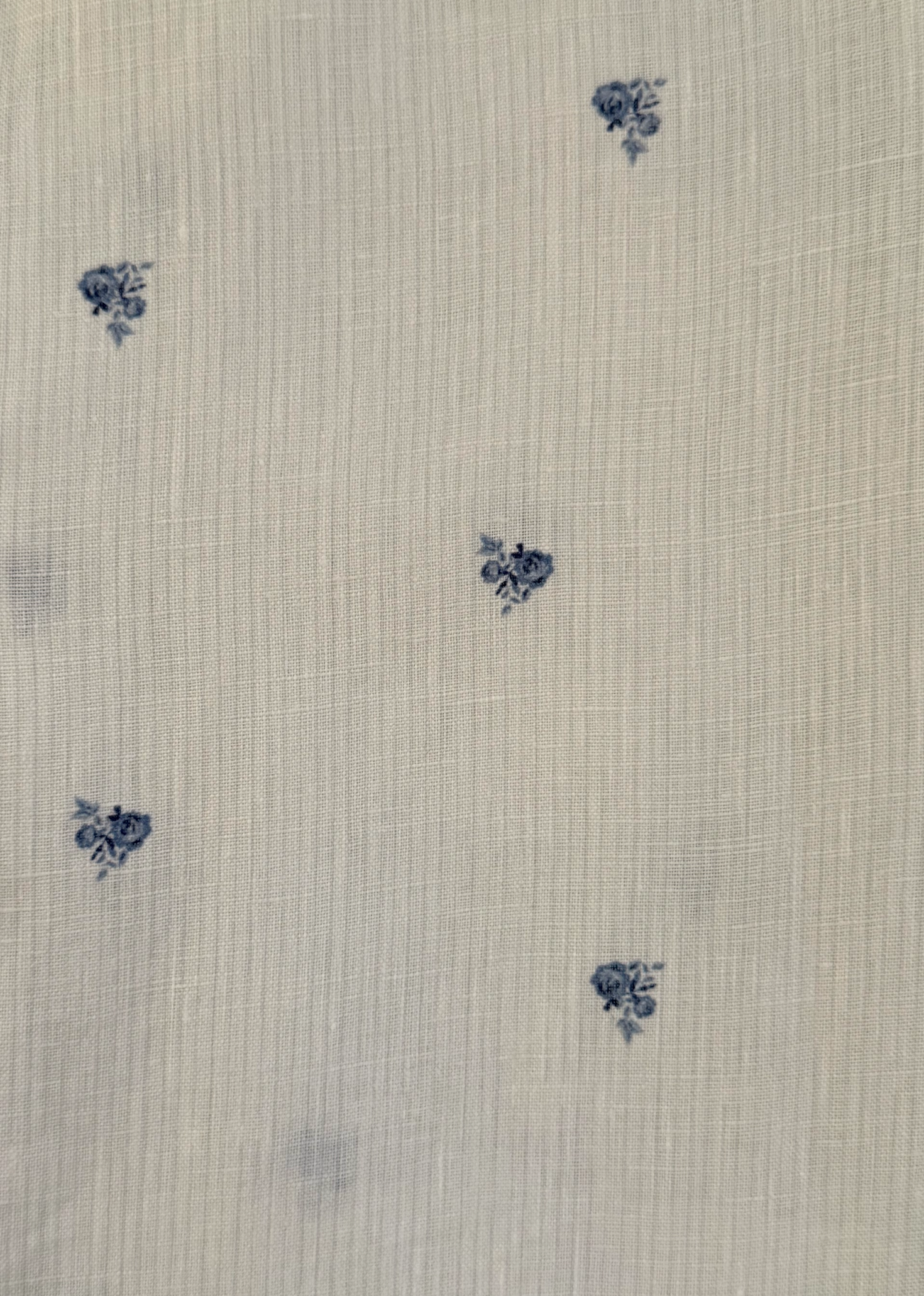 The Linen Ease Trouser - Floral Blue features a white fabric with a fine grid texture, adorned with an evenly spaced pattern of subtle small blue floral clusters. Inspired by Deiji Studios, this piece embodies delicate and timeless charm, making it an elegant addition to your wardrobe.