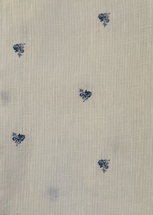 The Linen Ease Trouser - Floral Blue features a white fabric with a fine grid texture, adorned with an evenly spaced pattern of subtle small blue floral clusters. Inspired by Deiji Studios, this piece embodies delicate and timeless charm, making it an elegant addition to your wardrobe.