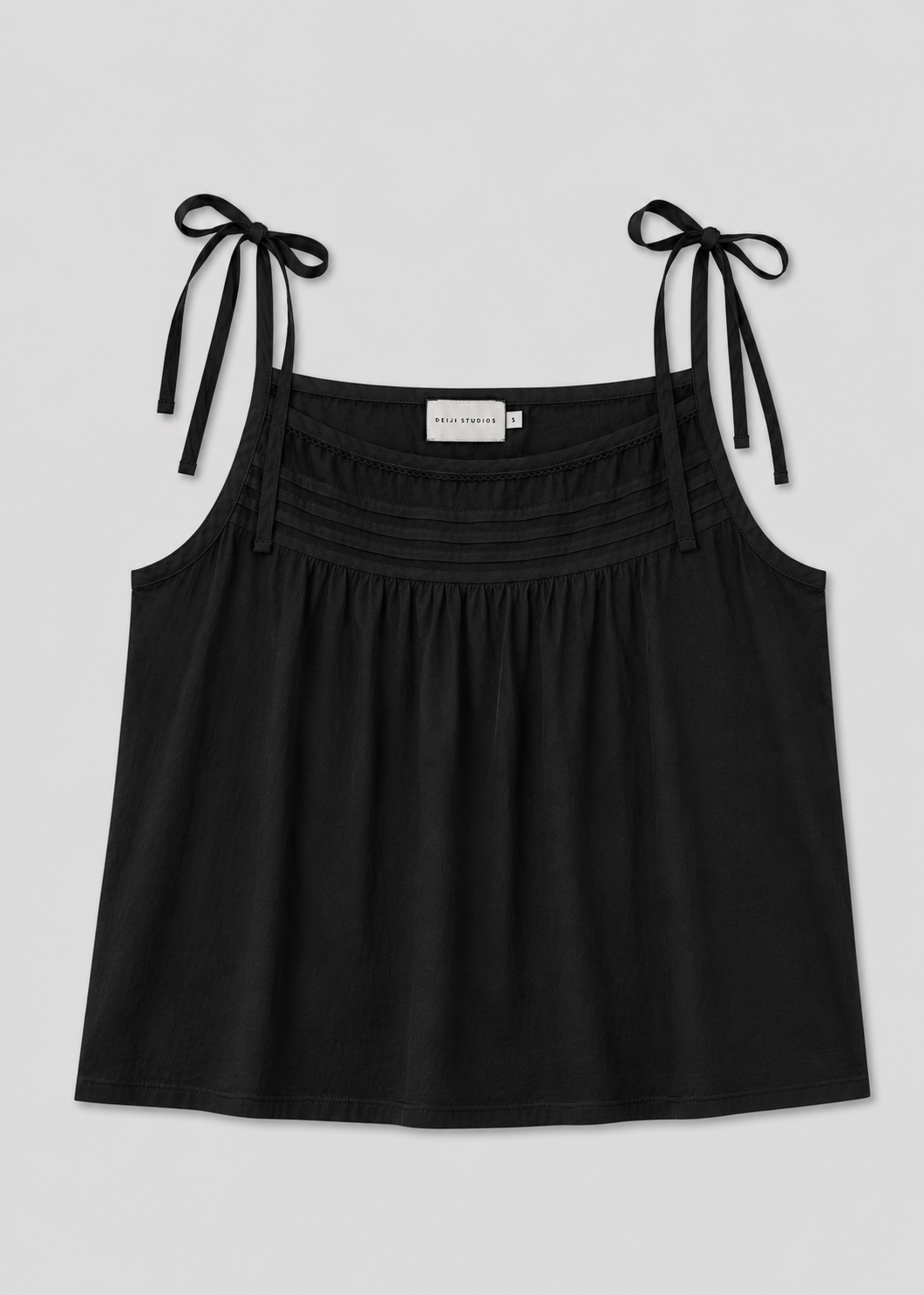 The Tied Cami - Black is a sleeveless top with tie shoulder straps, horizontal chest pleats, and a loose, flowy fit, capturing the relaxed style of Deiji Studios. The label inside reads Willow Strands.