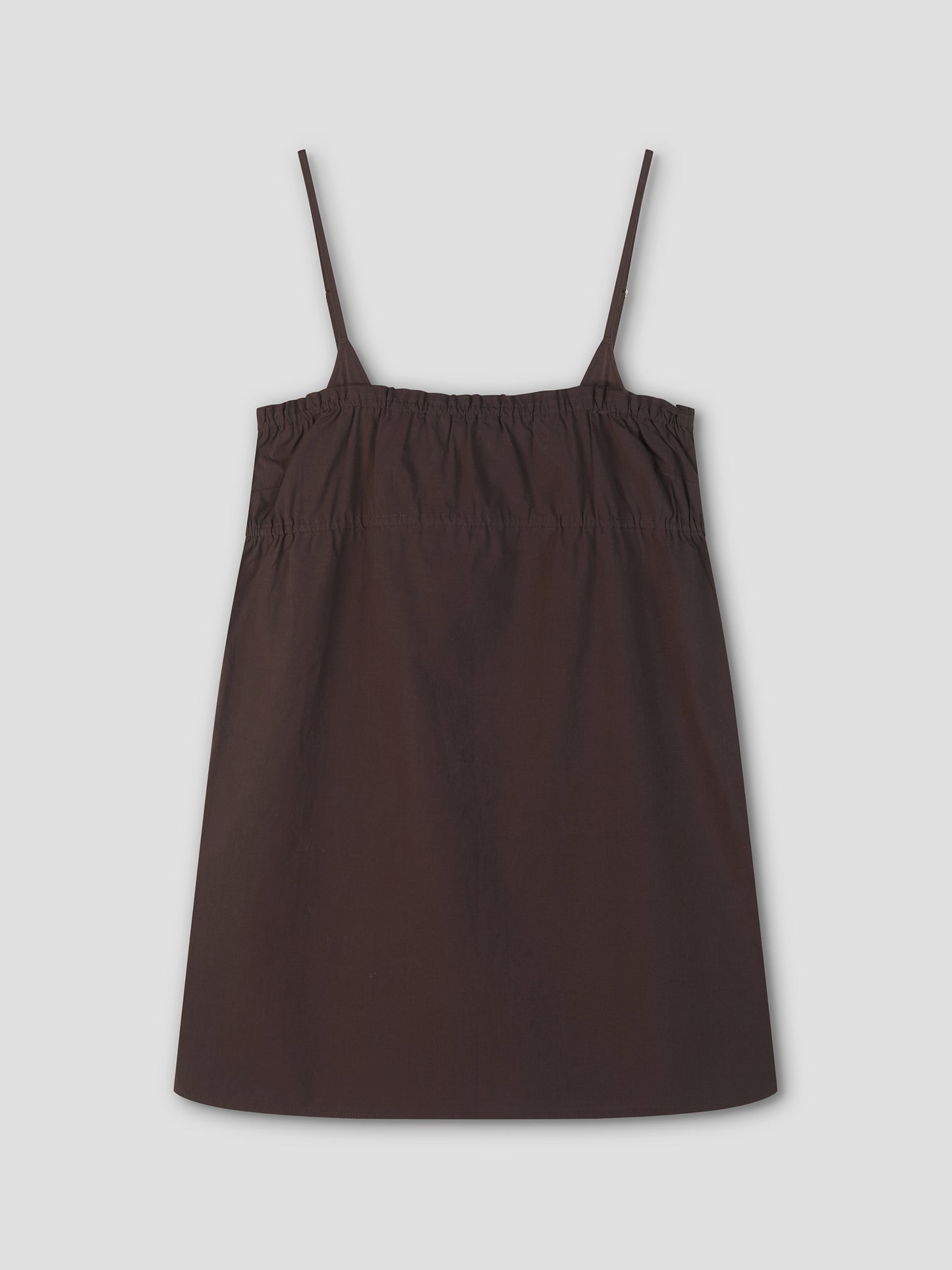 The Edge Dress - Sepia from Deiji Studios is a sleeveless, dark brown A-line dress with thin spaghetti straps and a gathered, elasticized upper section, shown on a light gray background.