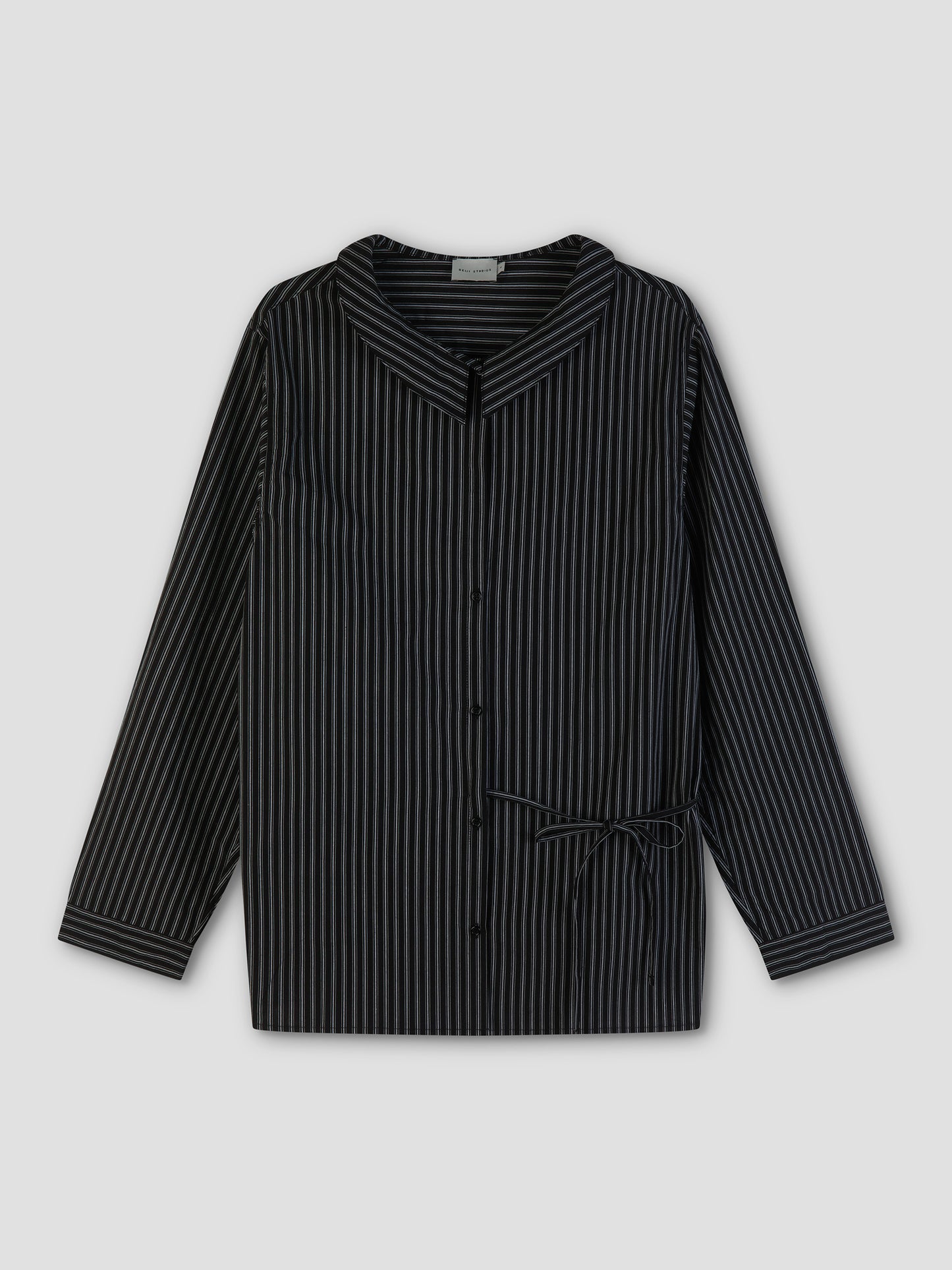 The Left Shirt is a black long-sleeve button-up with thin white vertical stripes, a wide collar, and a small side bow at the waist, shown laid flat on a plain gray background.