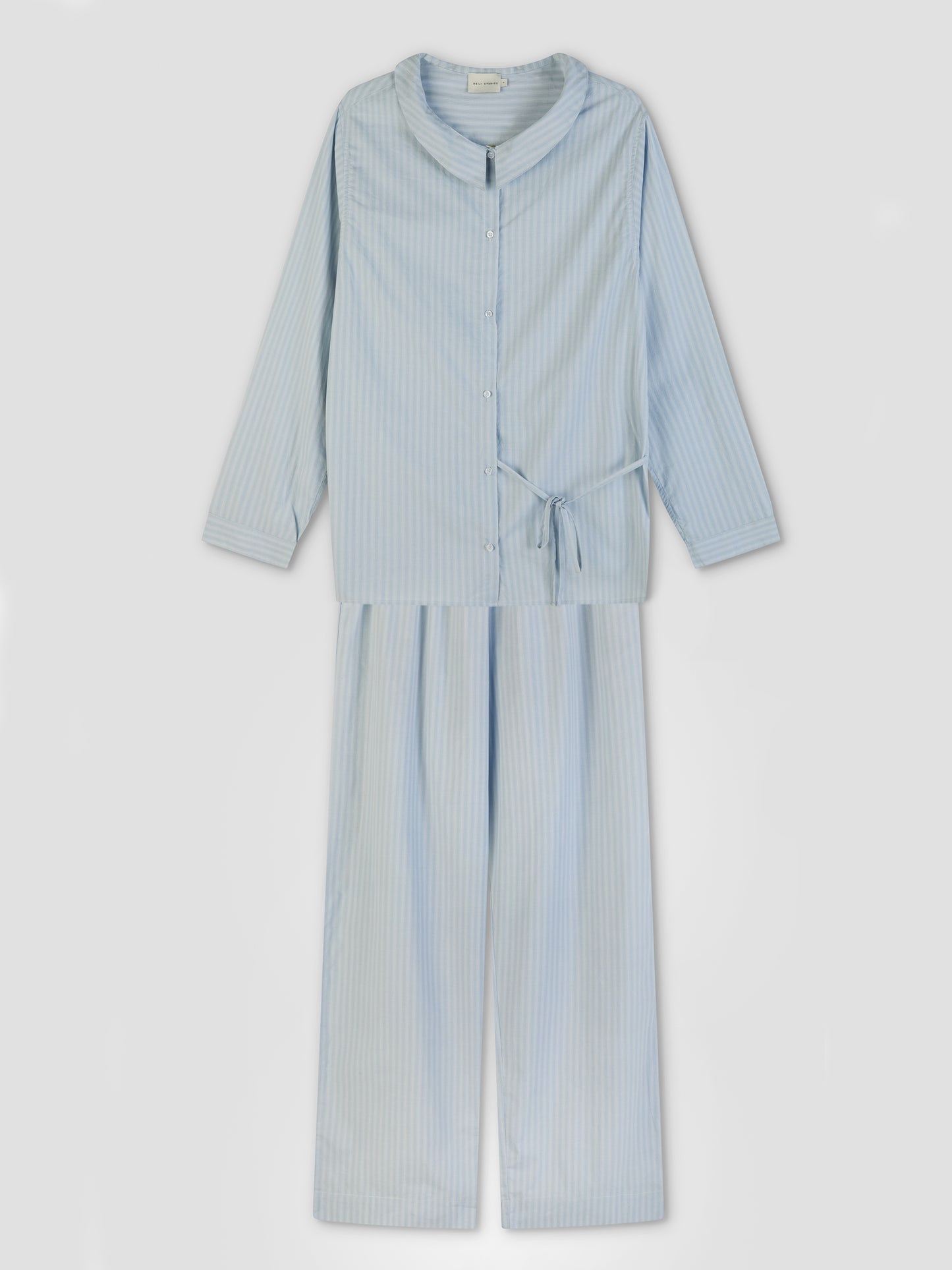 The Left Set - Lake Blue Stripe by Deiji Studios is a light blue and white striped long-sleeve pajama set with a relaxed fit, collared button-down shirt, waist tie, and wide-leg pants, shown laid flat on a plain background.