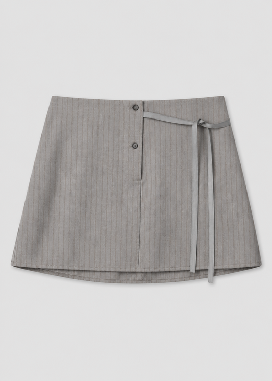 The Wool Tie Mini Skirt - Grey Stripe by Deiji Studios features a subtle wrap design, two front buttons, and a slim matching tie on the right side, shown against a white background.