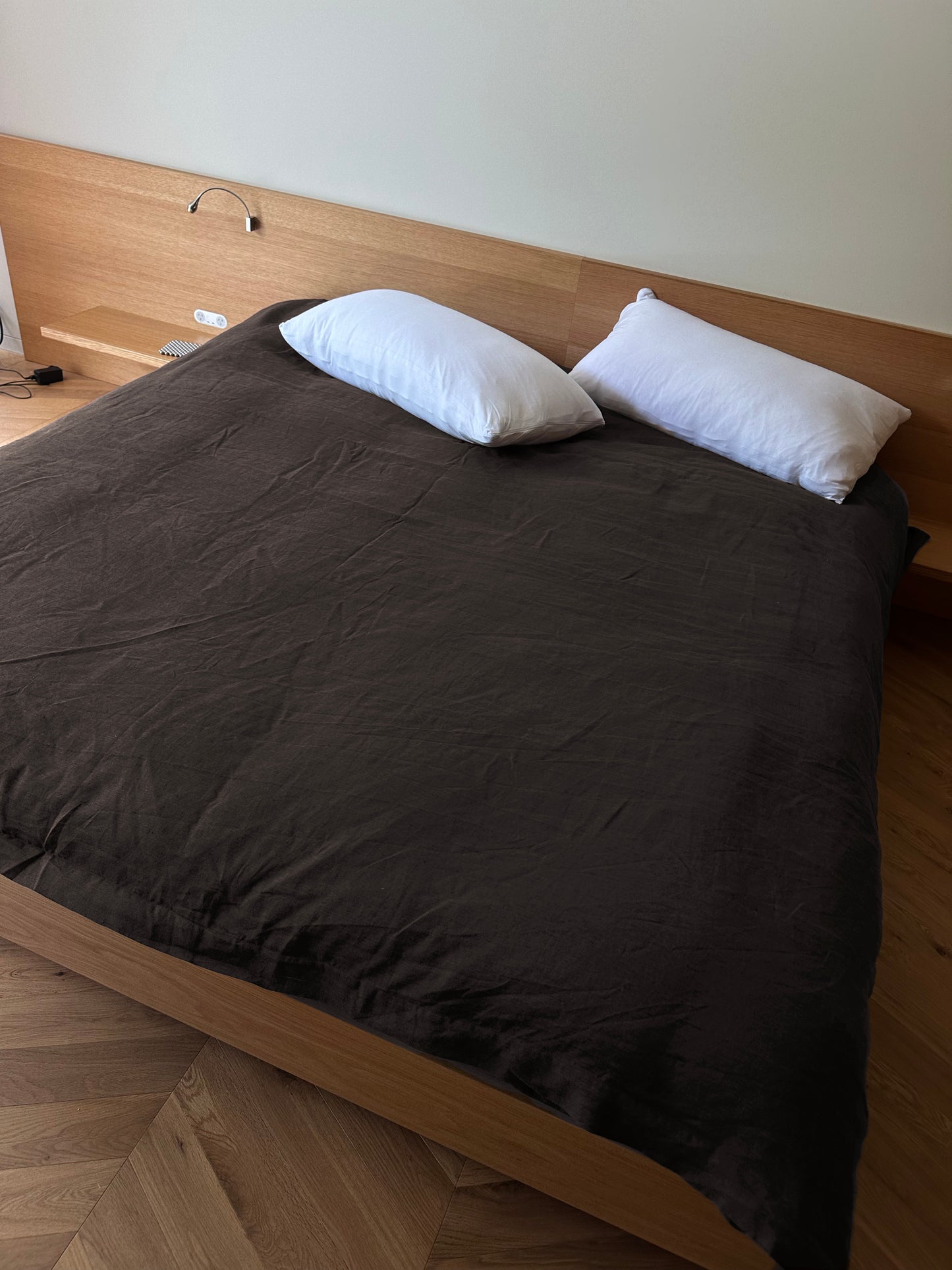 A neatly made bed with the Duvet cover - Bark and two white pillows, set against a wooden headboard in a modern minimalistic room with wooden flooring, features hypo-allergenic bedding for extra comfort.