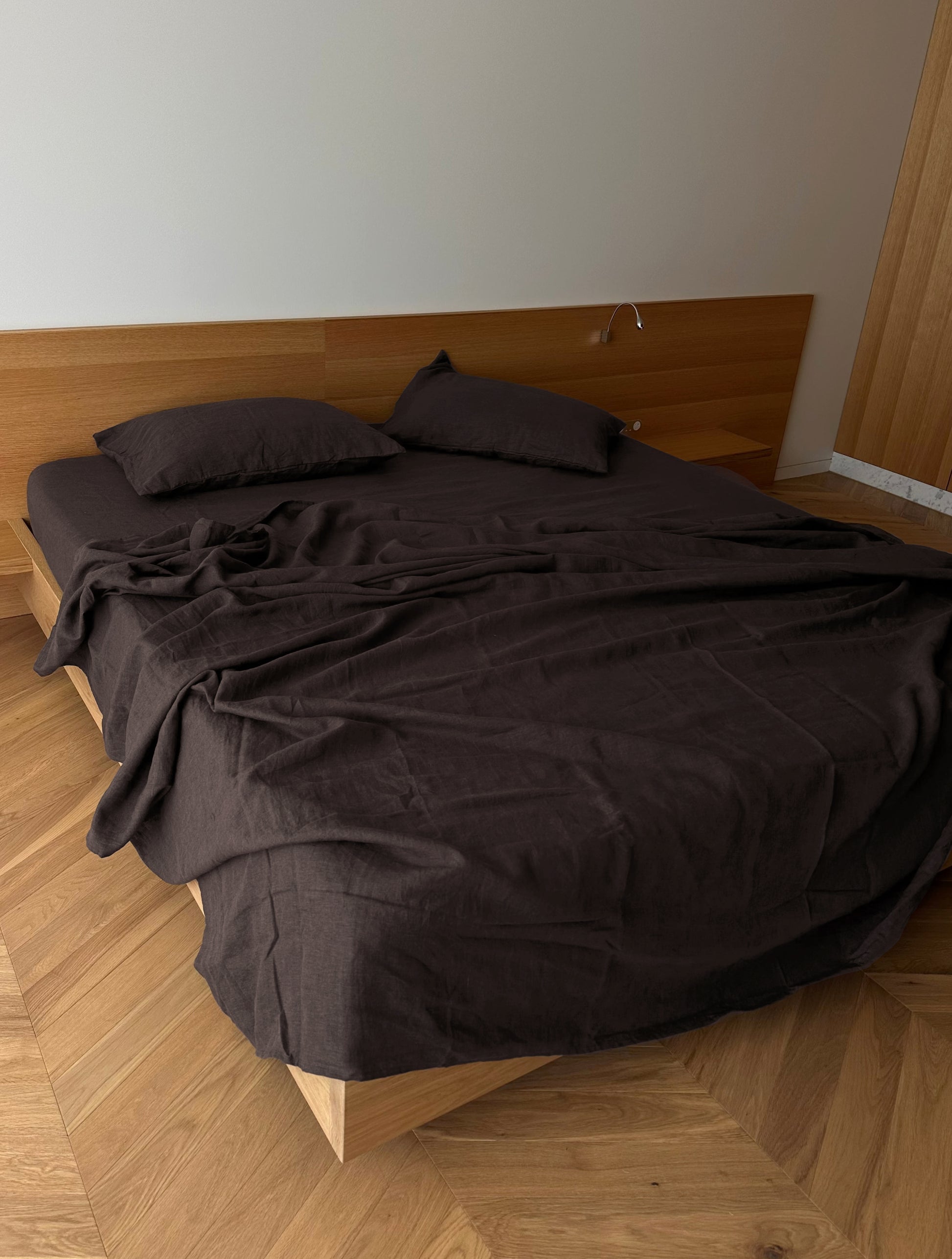 A double bed with eco-friendly Bark sheets and two pillows, set against a wooden headboard in a minimalist room with wooden flooring.