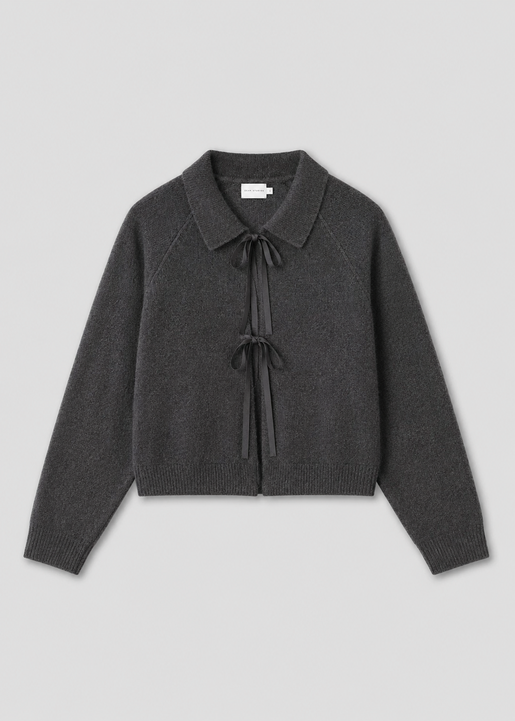 The Box Cardigan - Charcoal is a long-sleeved knit with a collar and two black ribbon ties on the front, inspired by Deiji Studios and shown on a light gray background.