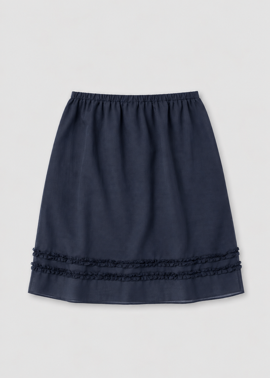 The Daytime Skirt - Navy by Deiji Studios laid flat against a plain white background, a cotton voile midi skirt in navy with a soft elasticated waistband, a straight silhouette and double frill detailing at the hem.