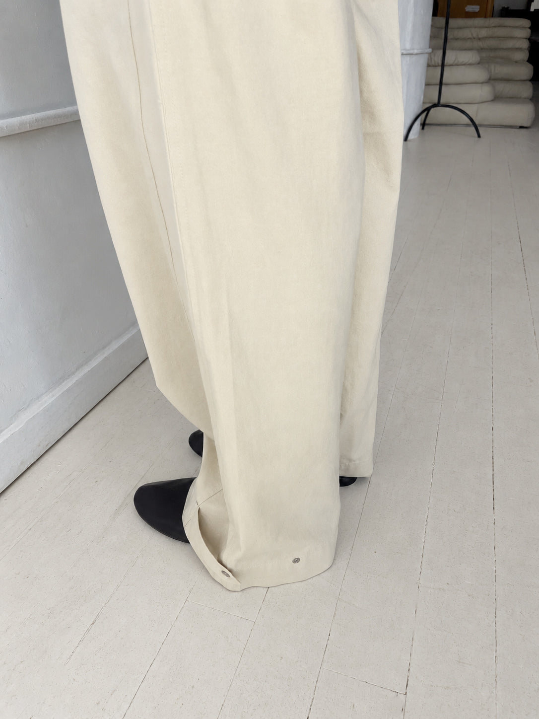 A close-up of the Snap Tab Pant - Stone by Deiji Studios, showing the wide-leg hem with its adjustable snap tab, worn with black shoes.