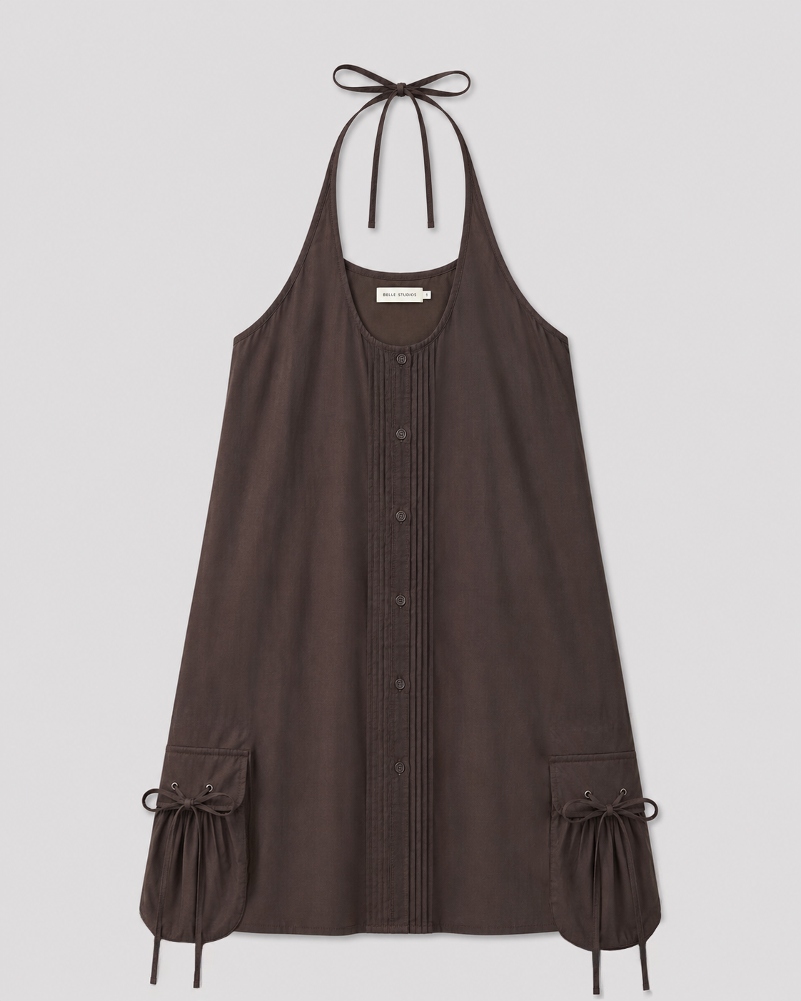 Pocket Halter Dress - Toast in dark brown, with a button-down front, vertical pleats, and gathered side pockets with drawstring ties near the hem, shown against a plain light background.
