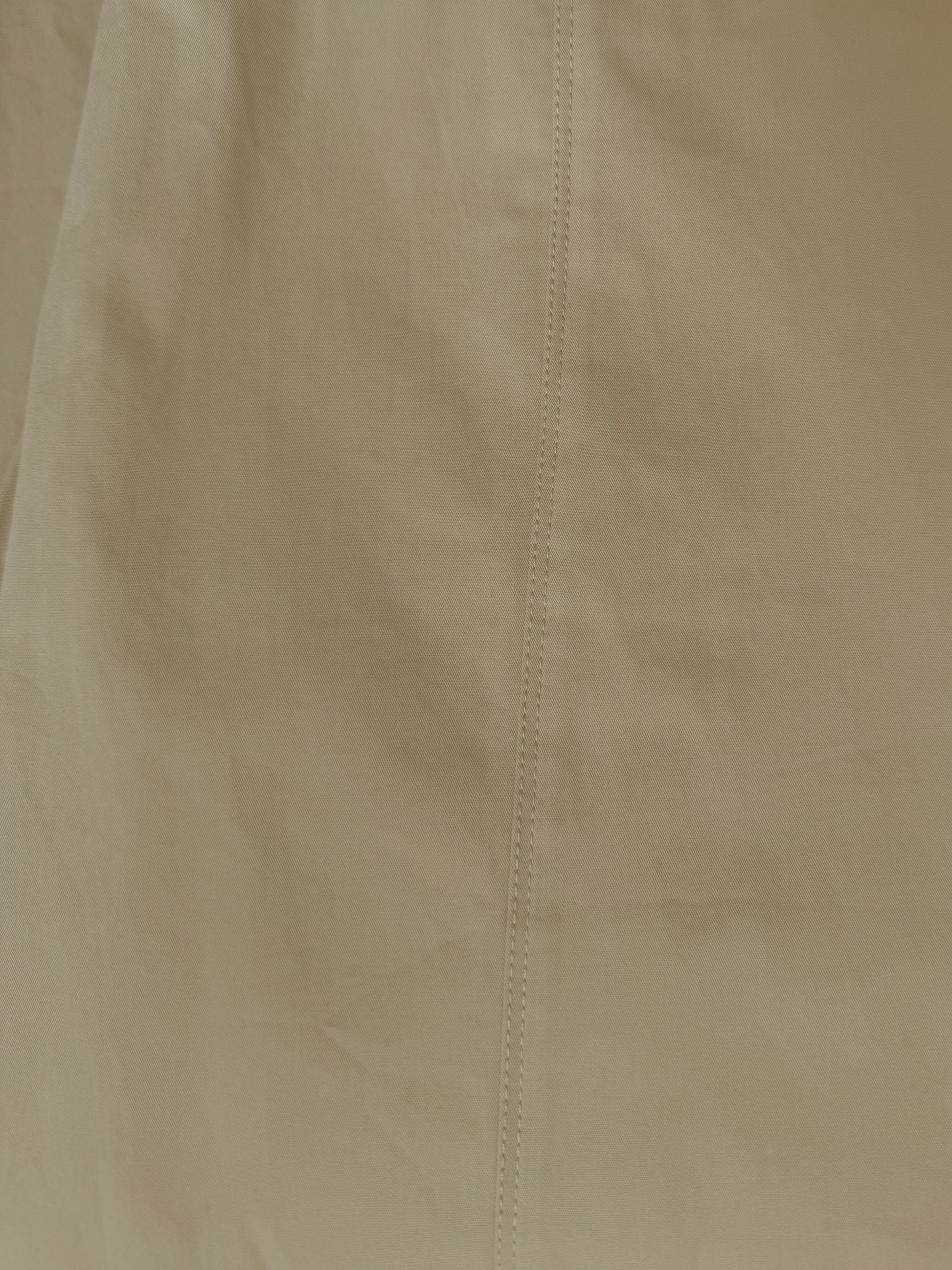 A close-up of the Pocket Pant - Stone by Deiji Studios shows beige organic cotton fabric with a vertical center seam, highlighting its texture and detailed stitching.