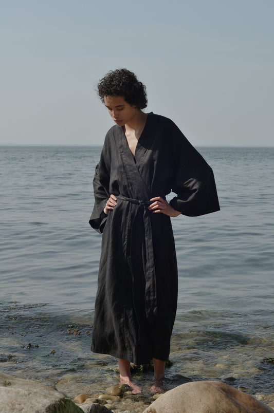 Female model wearing the 02 robe - deep black by Deiji Studios against ocean horizon