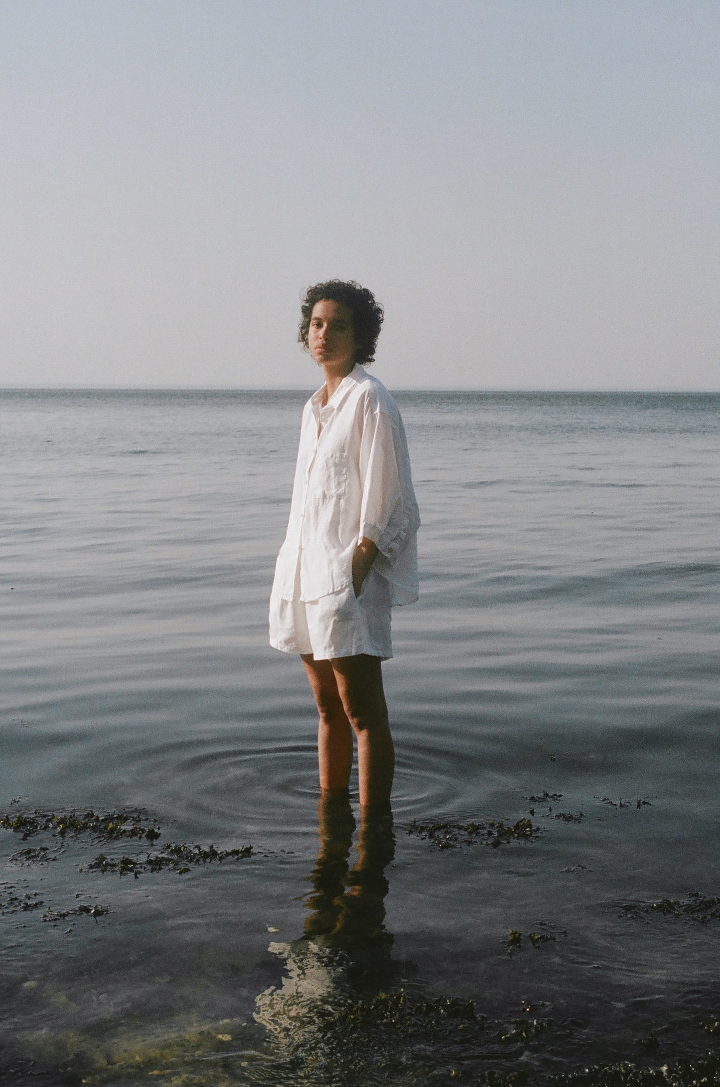 Female model wearing the 03 set - white by Deiji Studios against ocean horizon